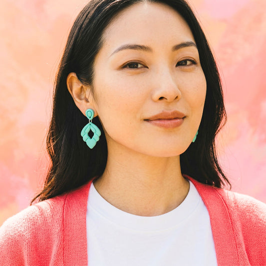 Woman wearing turquoise drop earrings with a pink and white background.