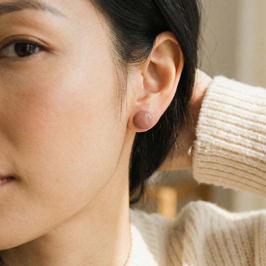 Close-up of a woman wearing blush coloured circular stud earrings with a blurred background.