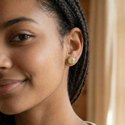 Close-up of a woman wearing round champagne gold stud earrings with a glossy finish against a blurred background.