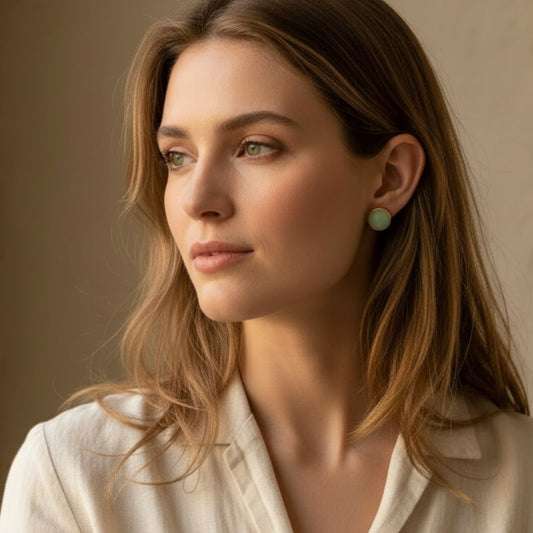 Woman wearing Australian handmade stud earrings in eucalyptus green with gold bezel against a neutral background.