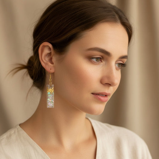 Woman wearing Australian handmade dangle earrings in transparent resin with gold leaf details and holographic shimmer.