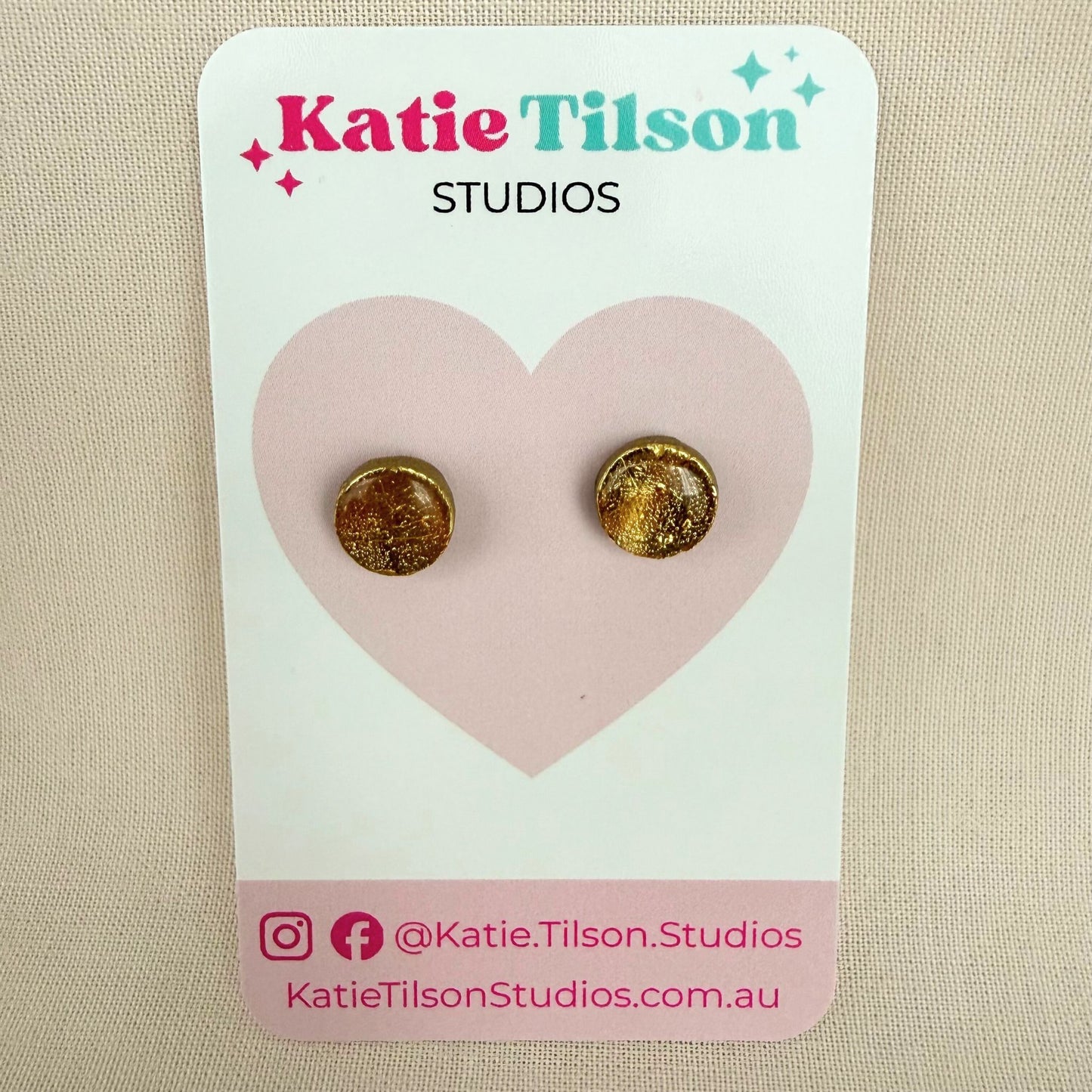 Gold round stud earrings on a Katie Tilson Studios card against a beige background.