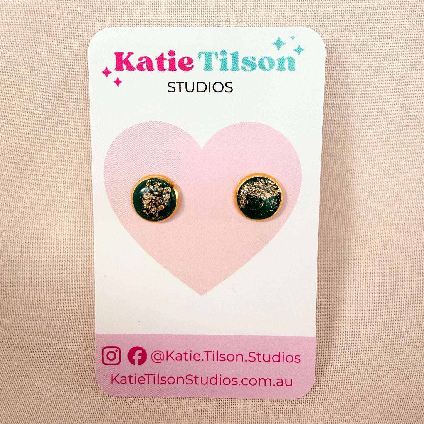 Emerald green circular studs with gold details on a Katie Tilson Studios card against a beige background.