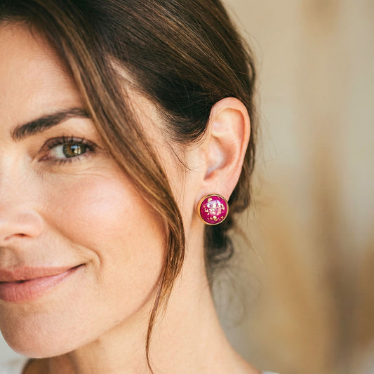 Good Vibes handmade stud earrings in magenta colour with gold flecks and gold bezel worn on woman's ear.