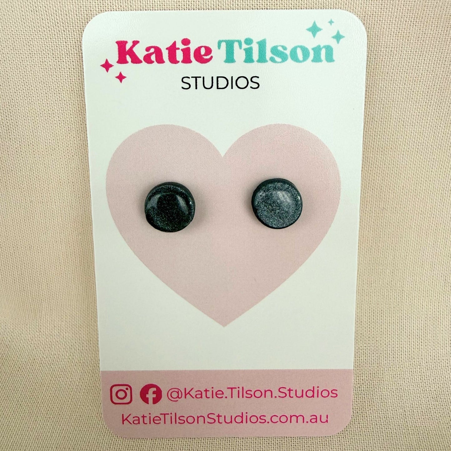 Graphite grey round stud earrings on a Katie Tilson Studios card against a beige background.
