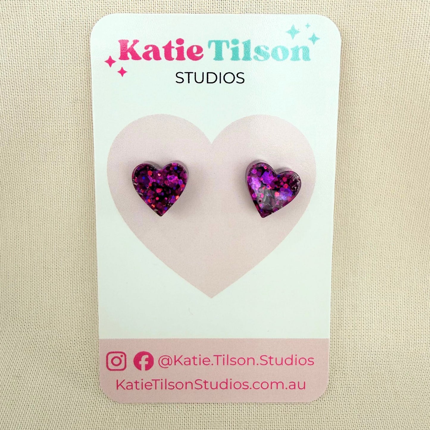 Purple resin glitter stud earrings on a Katie Tilson Studios card against a beige background.