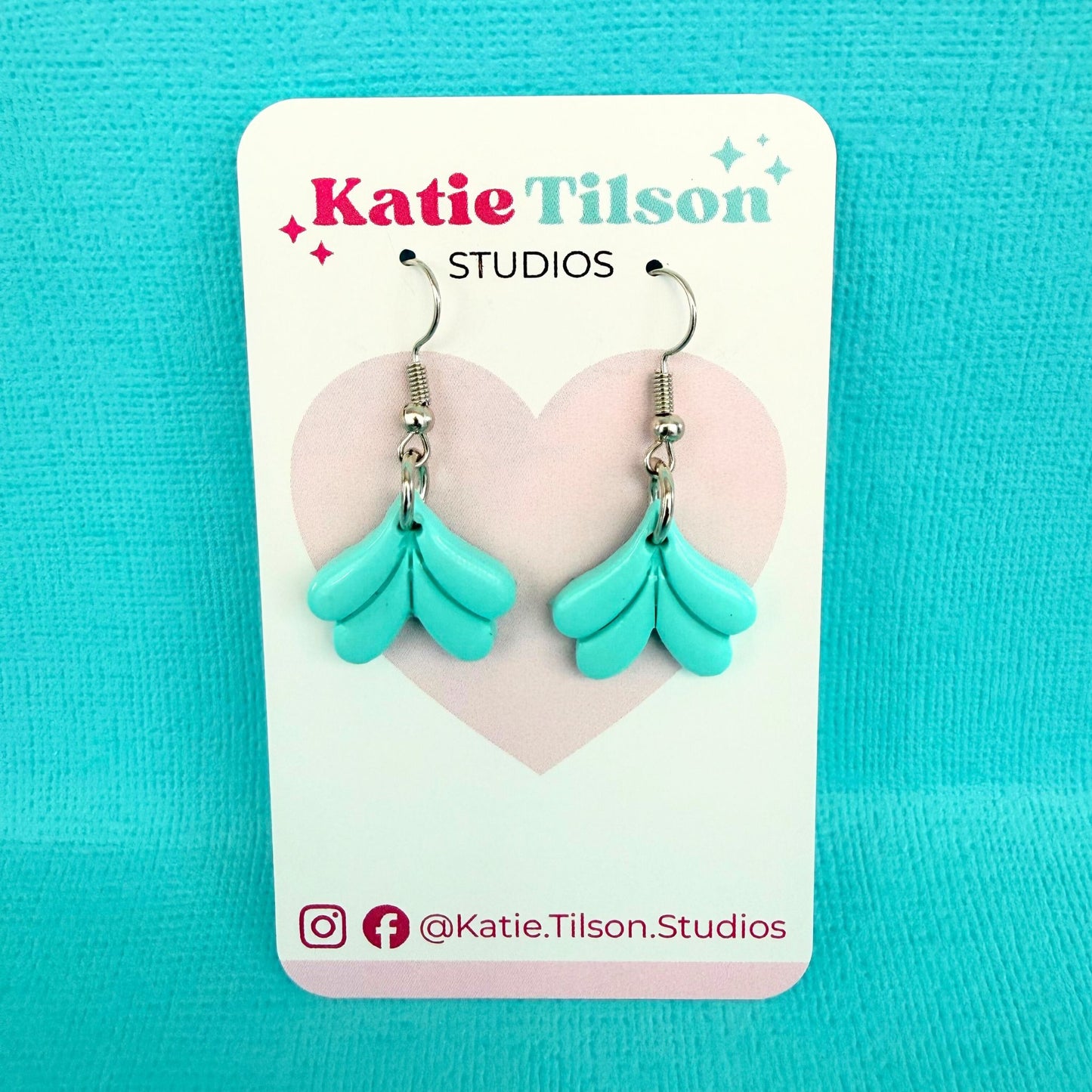 Turquoise dangle earrings on a Katie Tilson Studios card against a blue background.
