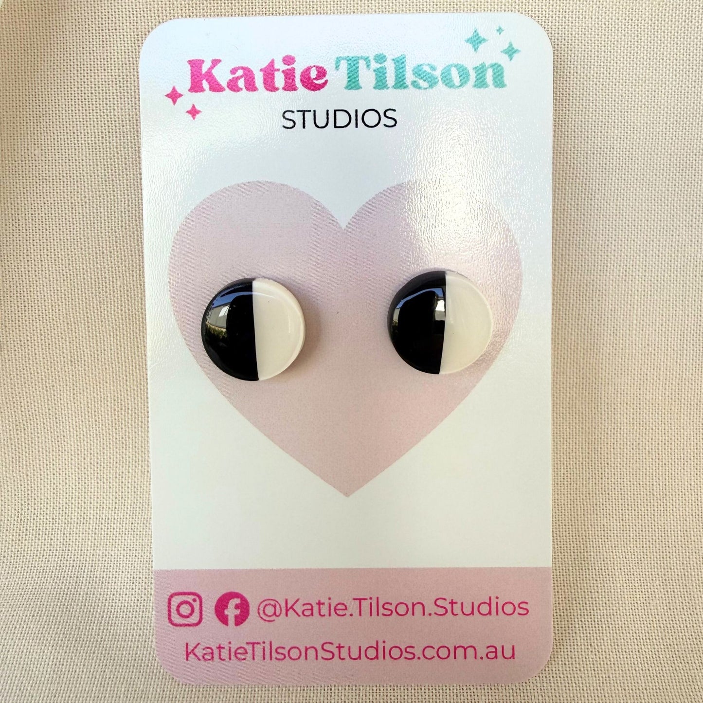 Black and white half and half circular stud earrings on a Katie Tilson Studios earring card against a beige background.