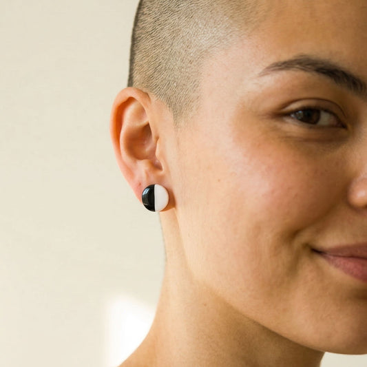 Close-up of a person wearing a black and white circular stud earring on a neutral background.