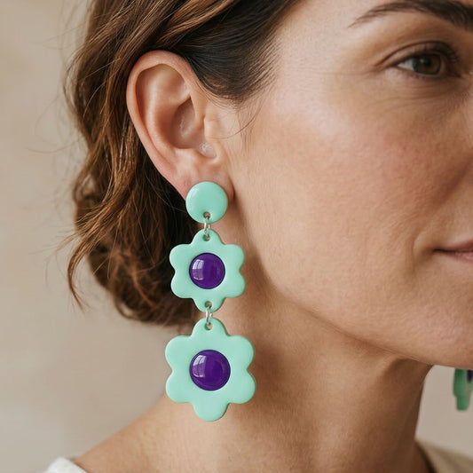 Close-up of a woman wearing mint flower-shaped dangle earrings with purple centers.