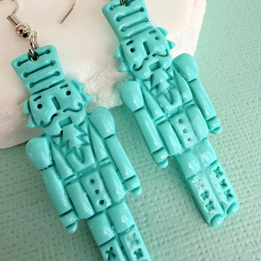 Turquoise nutcracker-shaped handmade dangle earrings on a light green background.