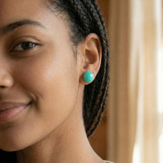 Close-up of a woman wearing round mint green stud earrings with a glossy finish against a blurred background.