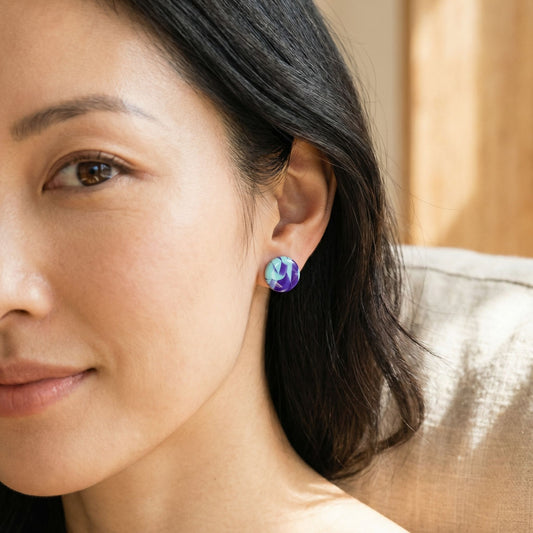 Close-up of a woman wearing purple and mint colorful abstract pattern circular stud earrings with a blurred background.