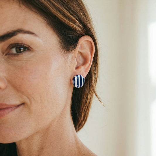 Close-up of a woman wearing a striped navy and white striped stud earring with a blurred background.