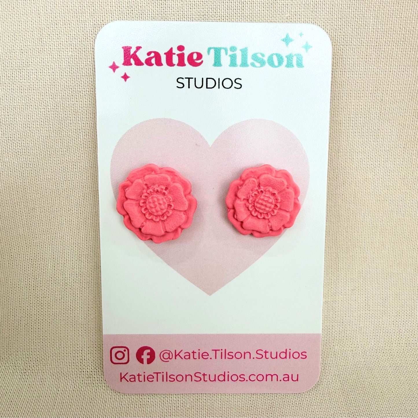 Blush coloured flower shaped stud earrings on a Katie Tilson Studios branded earring card resting against a beige background.