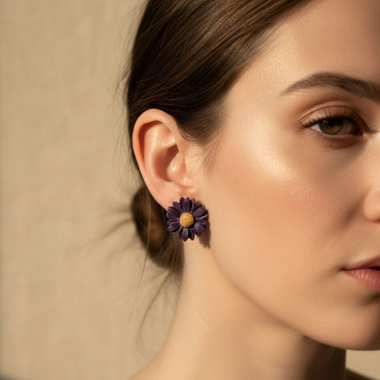 Close-up of a woman wearing a purple handmade flower stud earring with yellow centre against a neutral background.