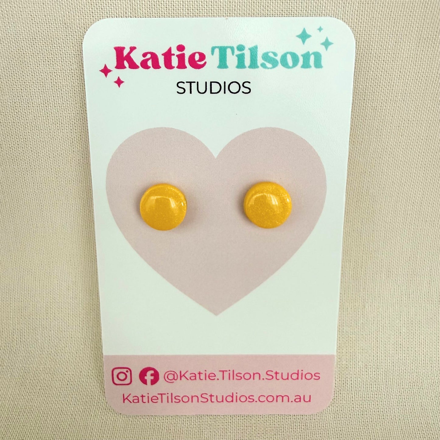 Yellow circular stud earrings on a Katie Tilson Studios card with a beige background.
