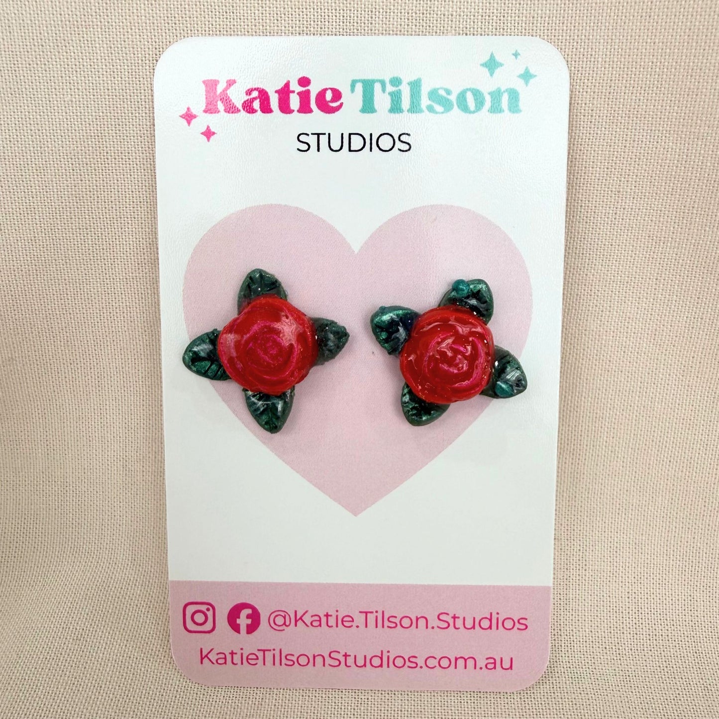 Red rose stud earrings on a Katie Tilson Studios card against a beige background.