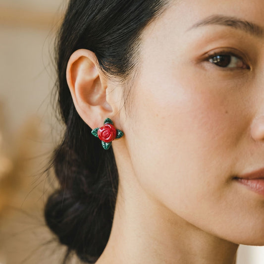 Close-up of a woman wearing red rose stud earrings with a blurred background.