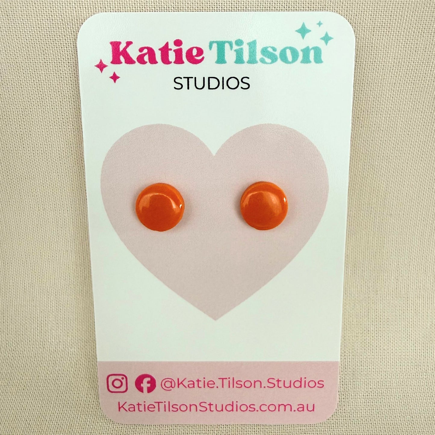 Orange circular stud earrings on a Katie Tilson Studios card.