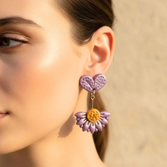 Close-up of a woman wearing purple flower-shaped polymer clay drop earrings with a blurred background.