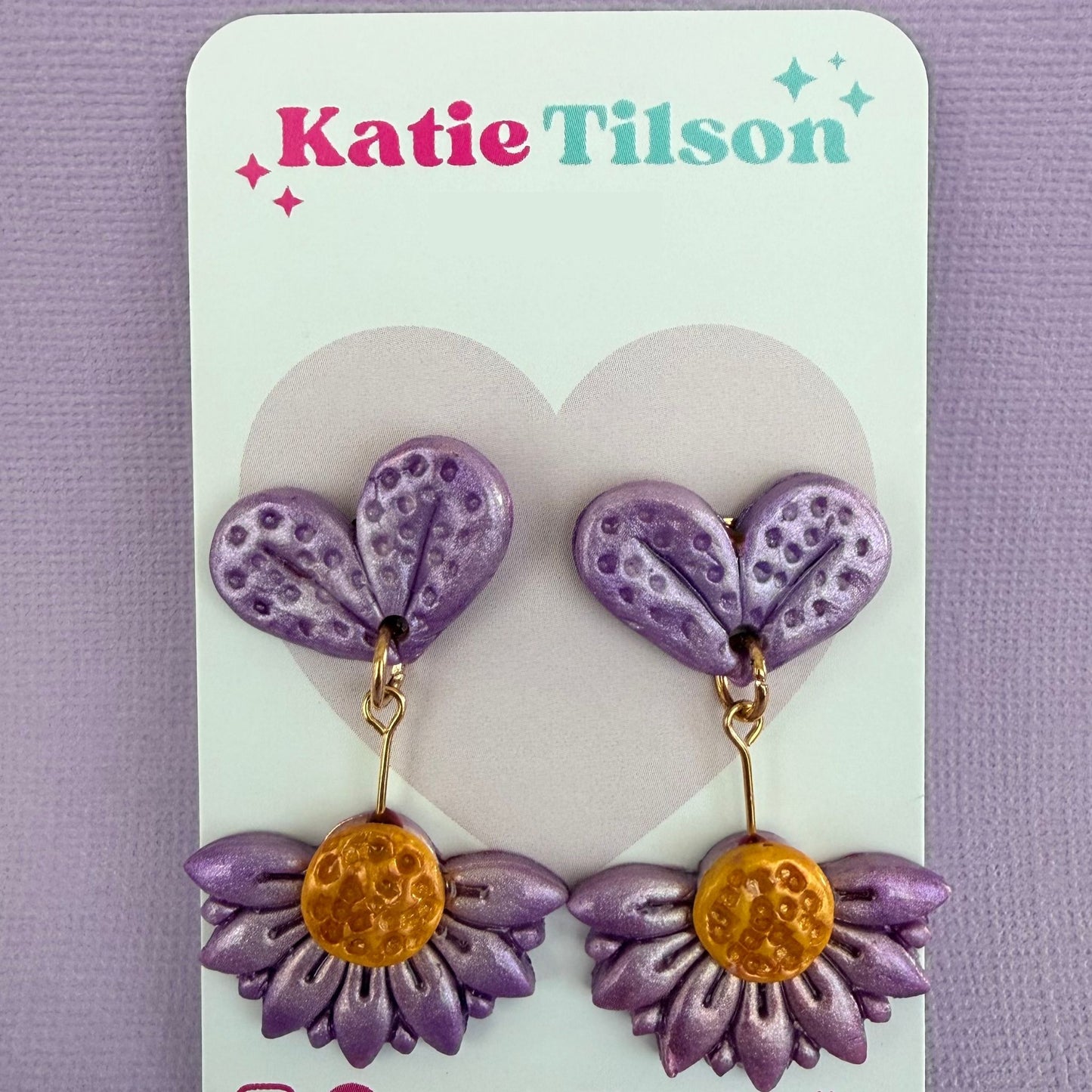 Purple and gold floral drop earrings on a Katie Tilson branded card against a purple background.