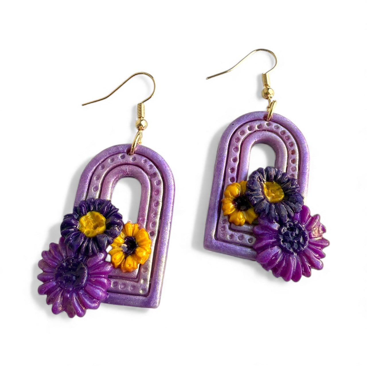 a pair of purple arch shaped polymer clay earrings with flower details on a white background