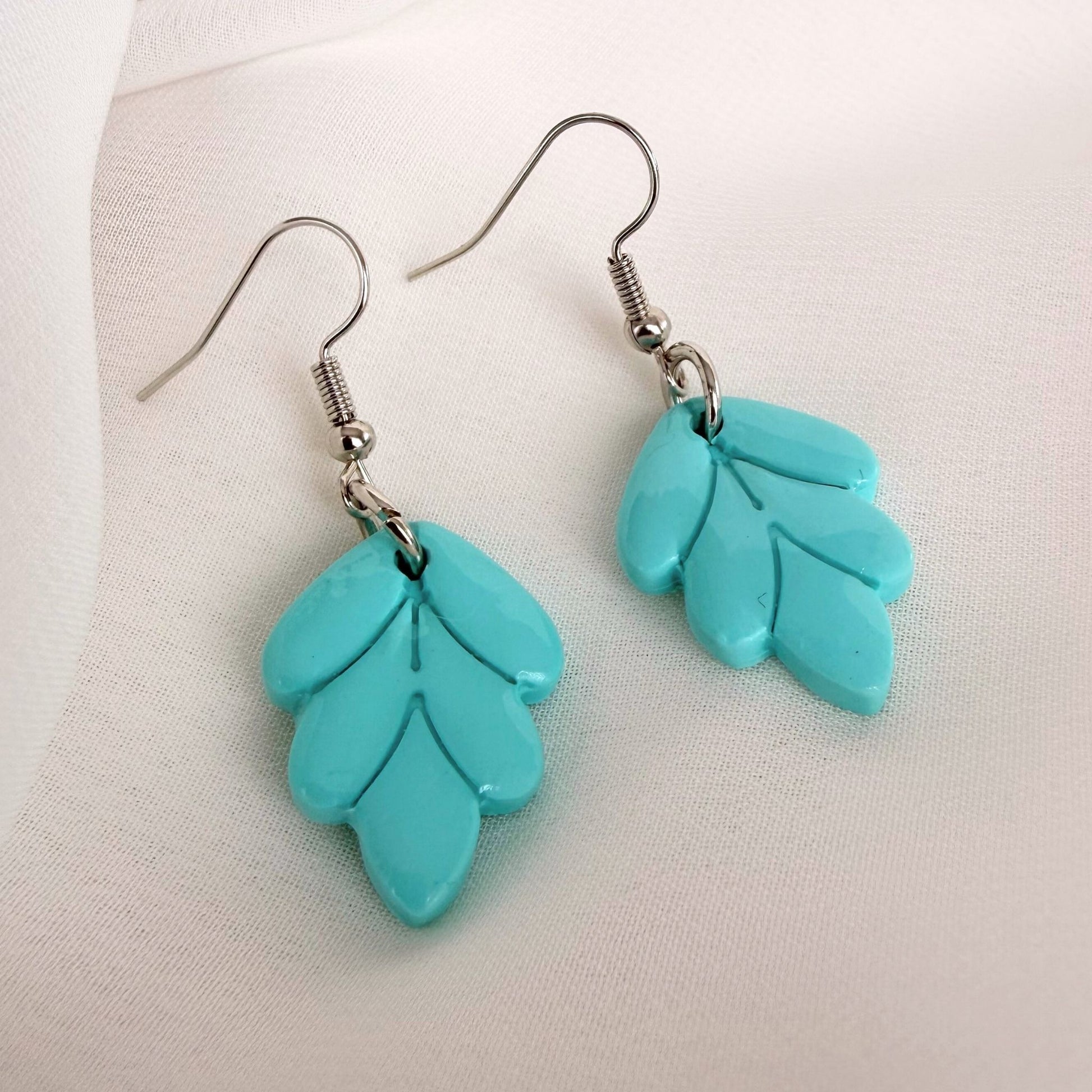 Australian handmade dangle earrings Aqua Leaf styled on white fabric