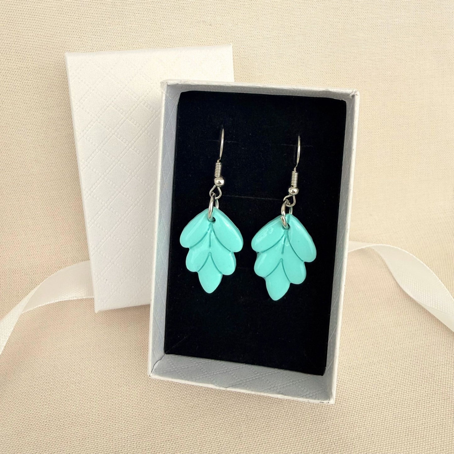 Aqua Leaf handmade dangle earrings in leaf design resting on black velvet insert inside a white gift box.