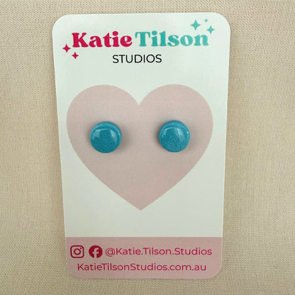 Aqua blue circular stud earrings on a Katie Tilson Studios card against a beige background.