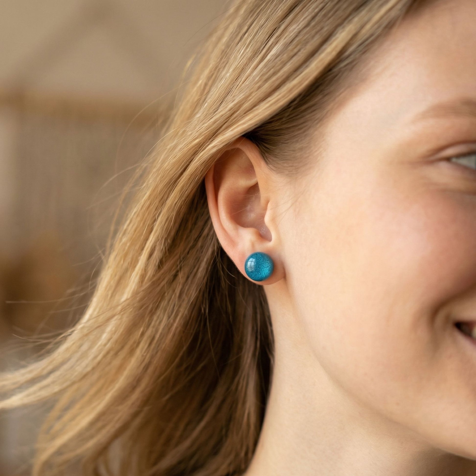 Close-up of a woman wearing a round aqua earring with a glossy finish against blurred background.