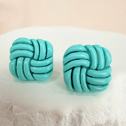 Aqua knotted stud earrings on a textured white surface with a light beige background.