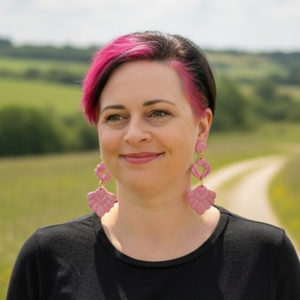 Portrait of jewellery artist Katie Tilson wearing her own handmade earrings standing in a field