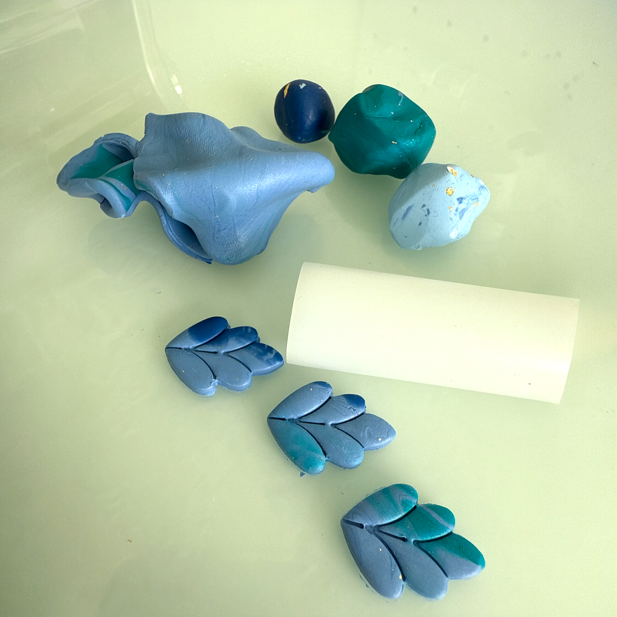 blue and teal polymer clay pieces and tools resting on a white benchtop