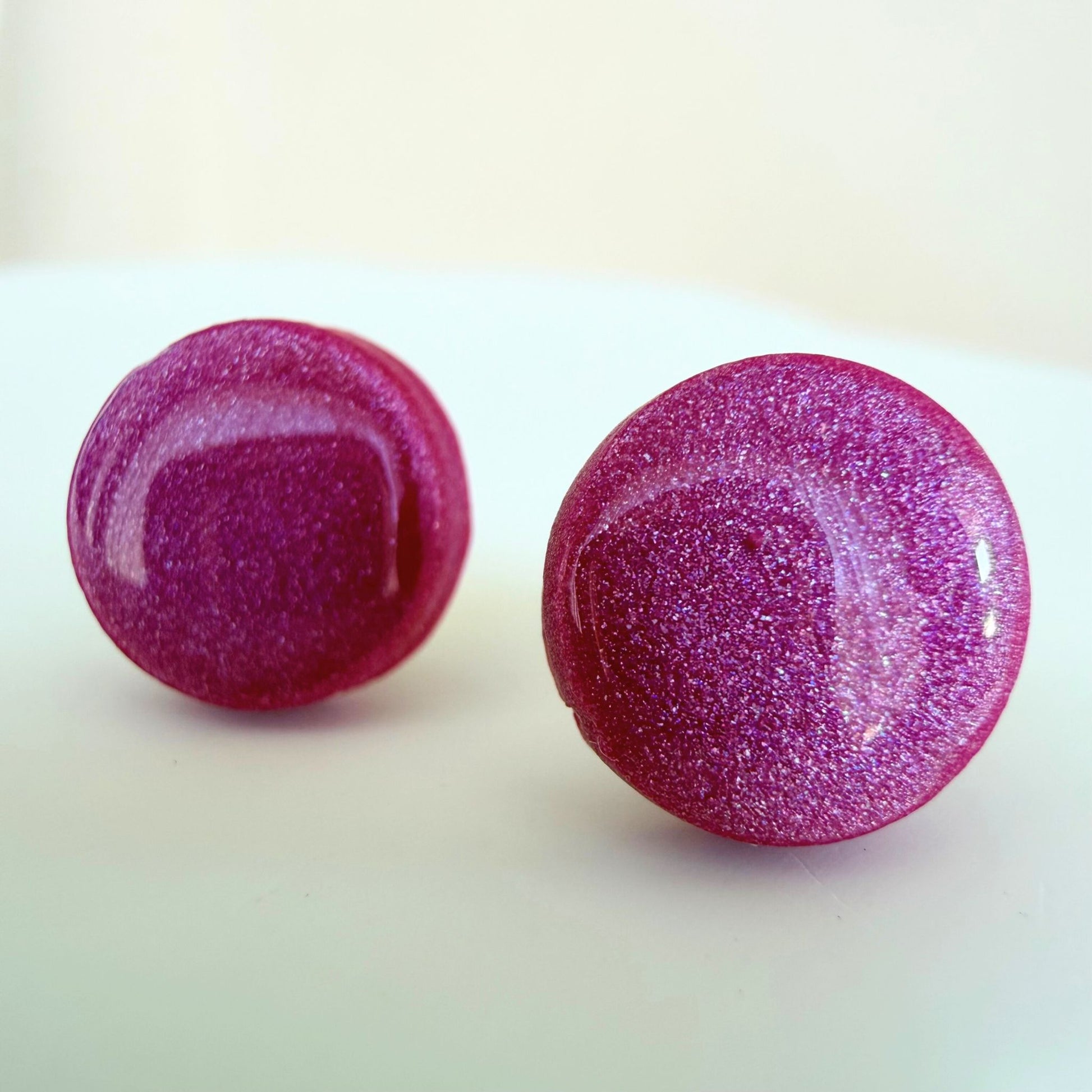 Pair of berry coloured glittery round stud earrings on a white background.