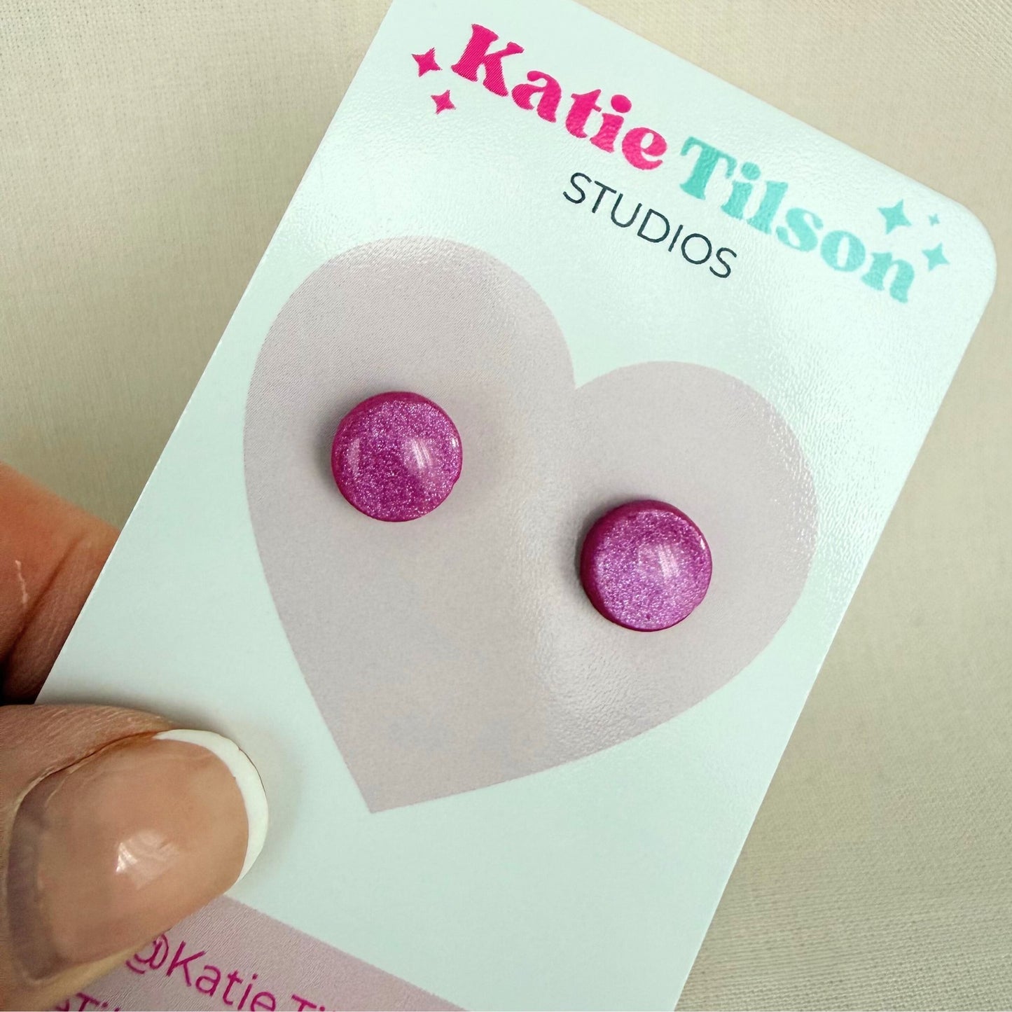 Berry coloured stud earrings on a Katie Tilson Studios card with a hand holding the card.