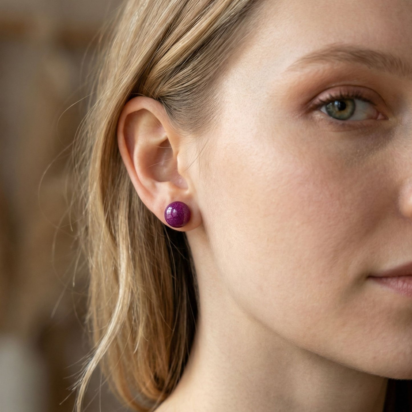 Close-up of a woman wearing berry coloured circular stud earrings with a blurred background.