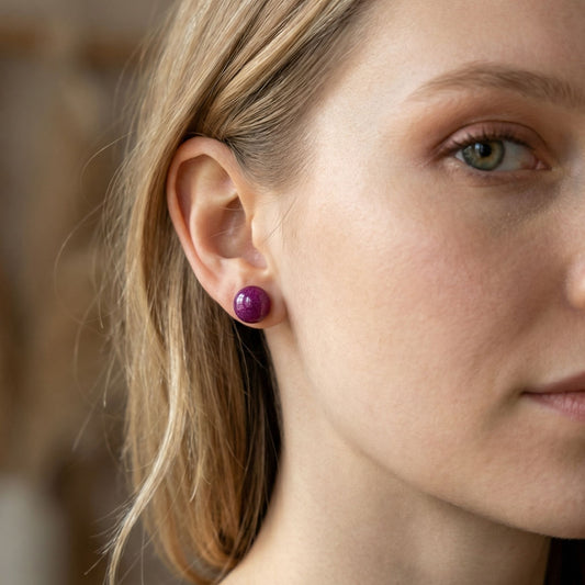 Close-up of a woman wearing berry coloured circular stud earrings with a blurred background.