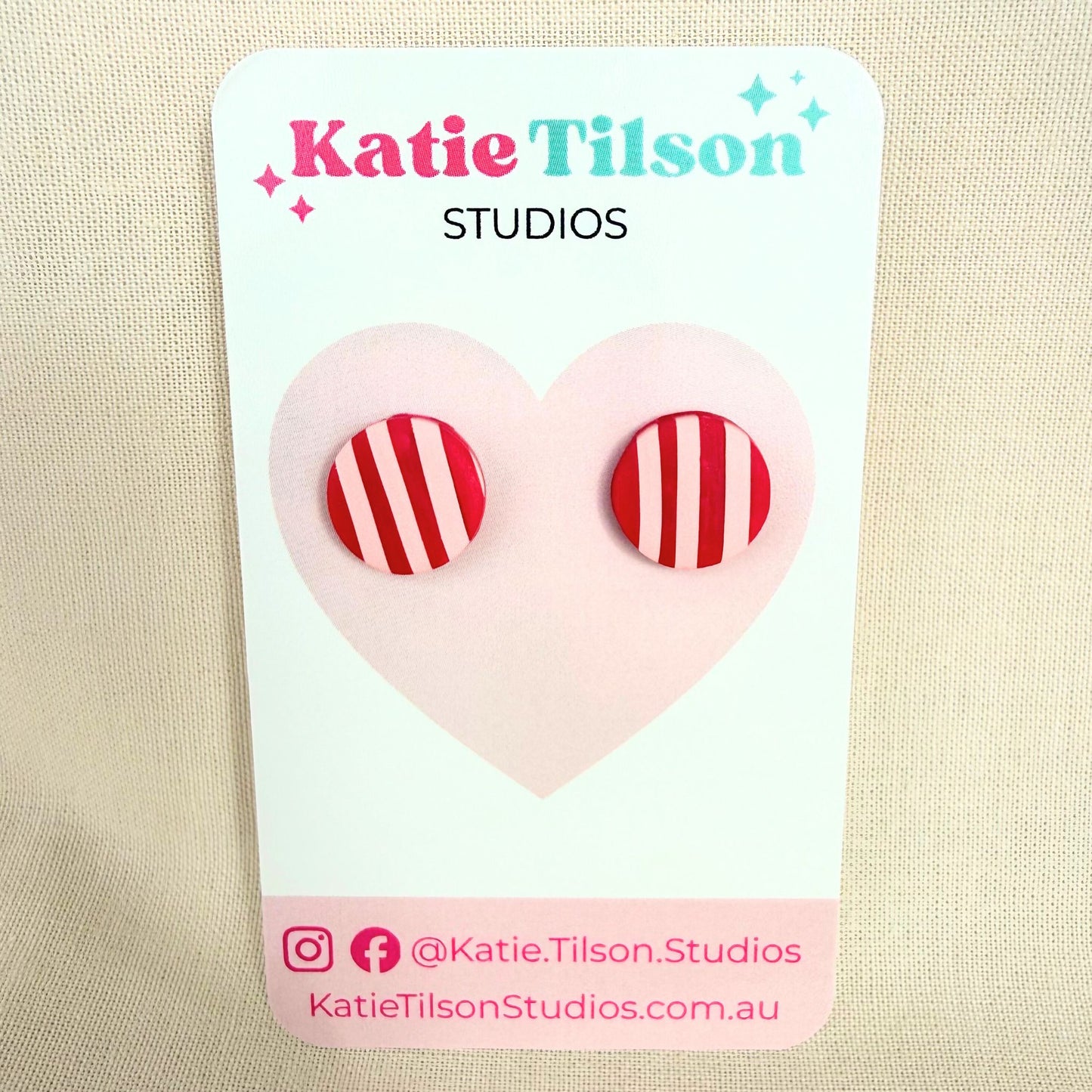 Katie Tilson Studios handmade stud earrings in pink stripe design on a branded earring card against a beige background.
