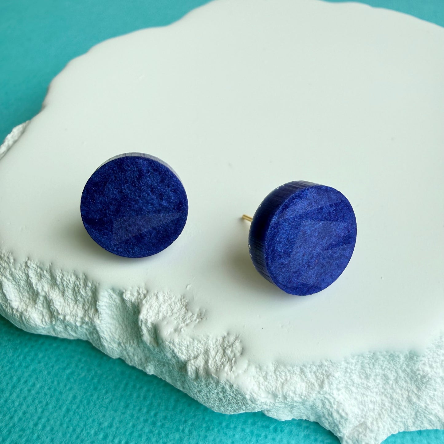 Blue round resin holographic shimmer earrings on a decorative white plate with a light blue background