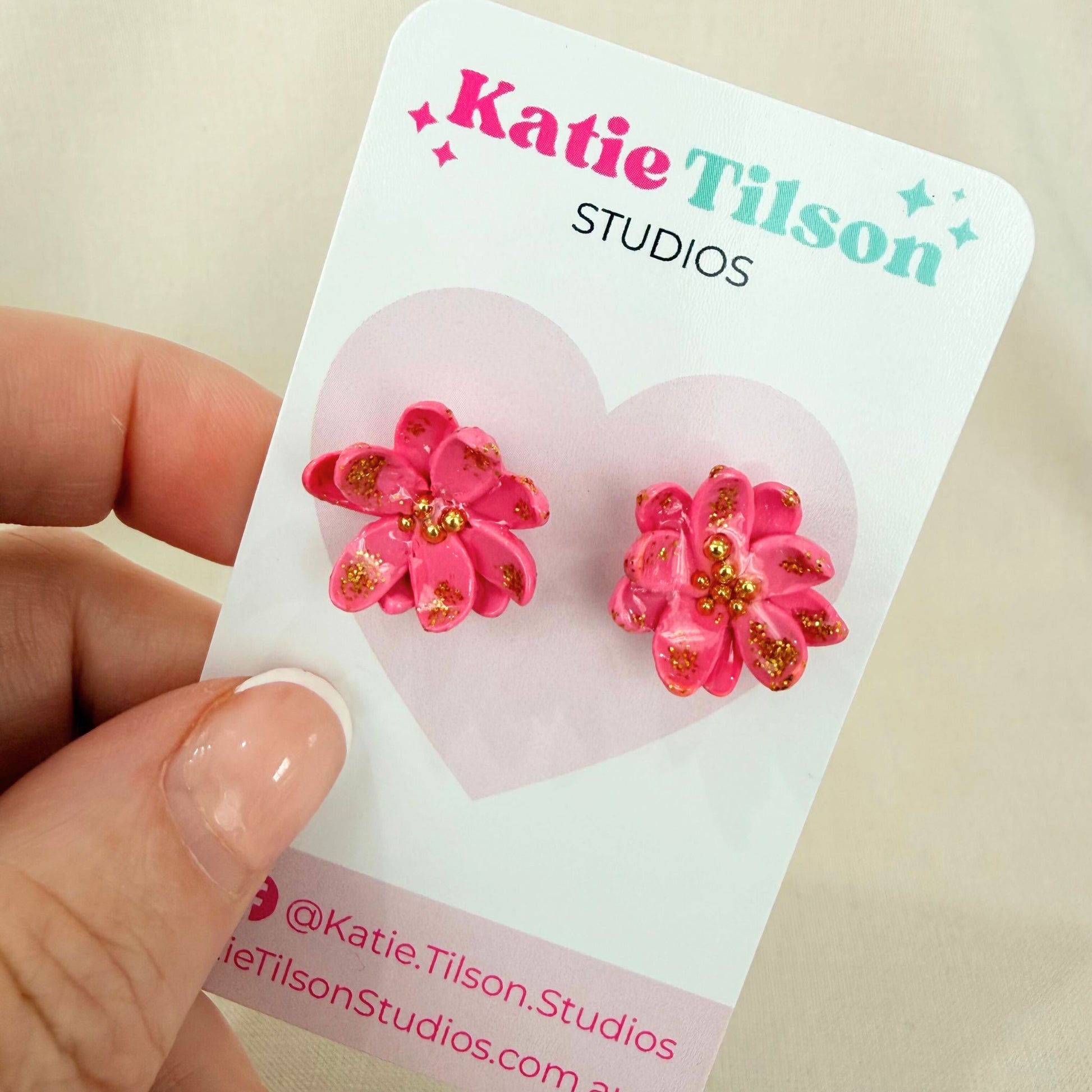 Pink flower stud earrings on a Katie Tilson Studios card held by a hand.