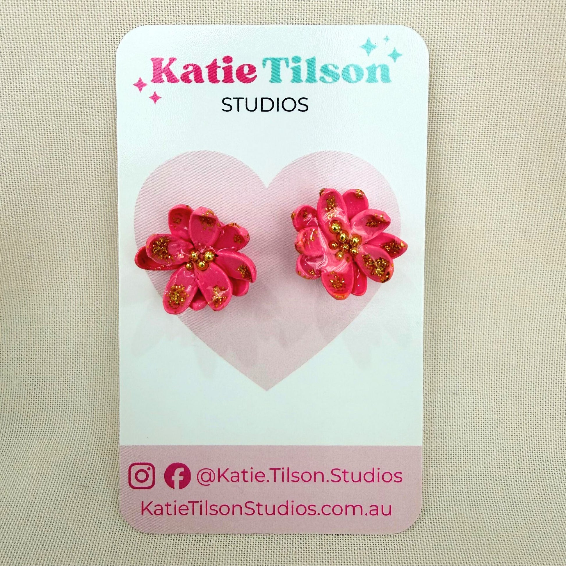 Pink floral stud earrings on a Katie Tilson Studios card with a beige background.