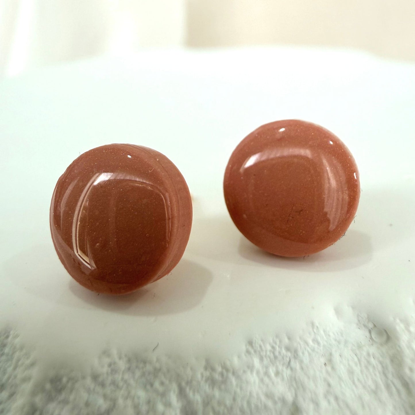 Pair of blush pink circular earrings stud on a textured white surface.