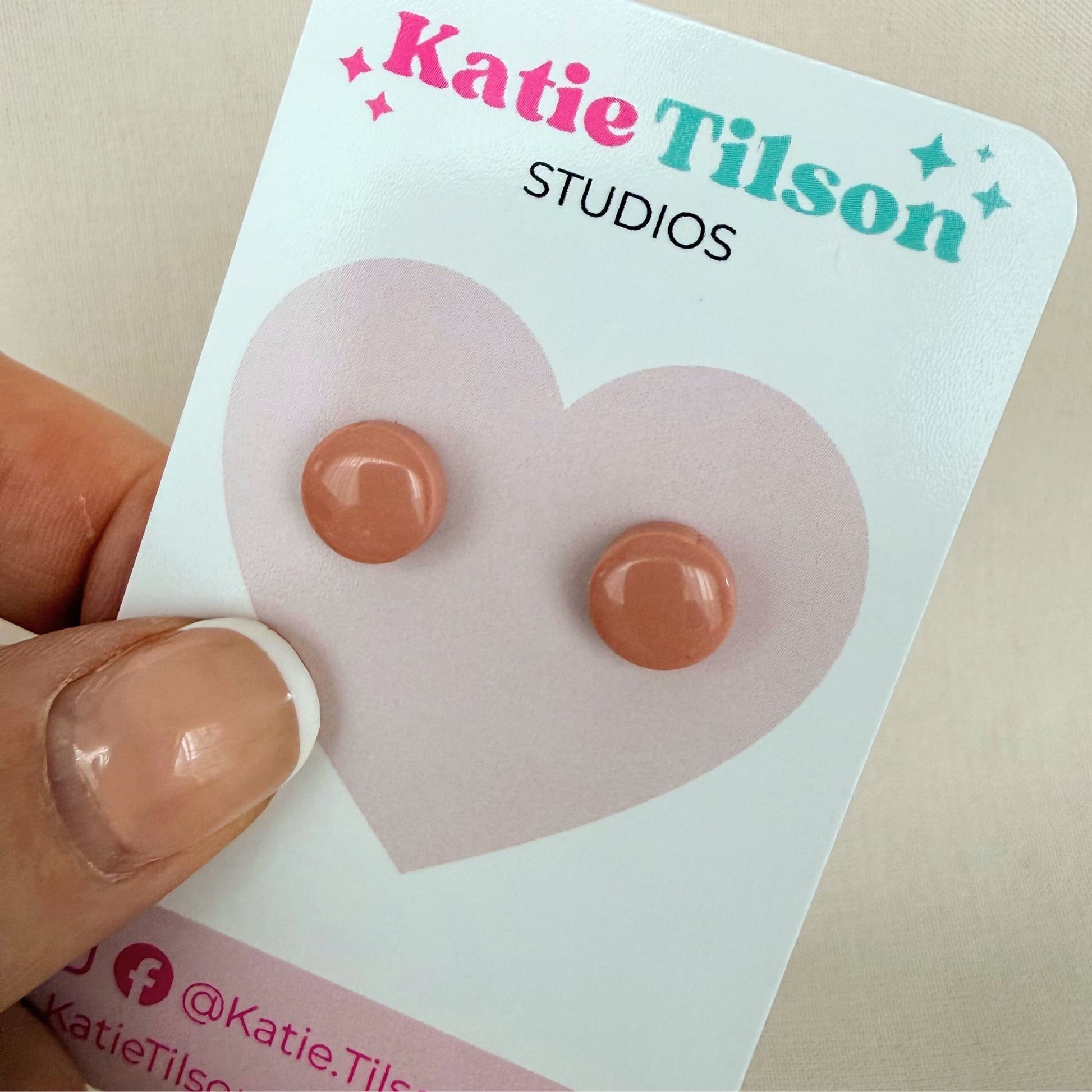 Blush coloured round stud earrings on a Katie Tilson Studios earring card held by a hand.