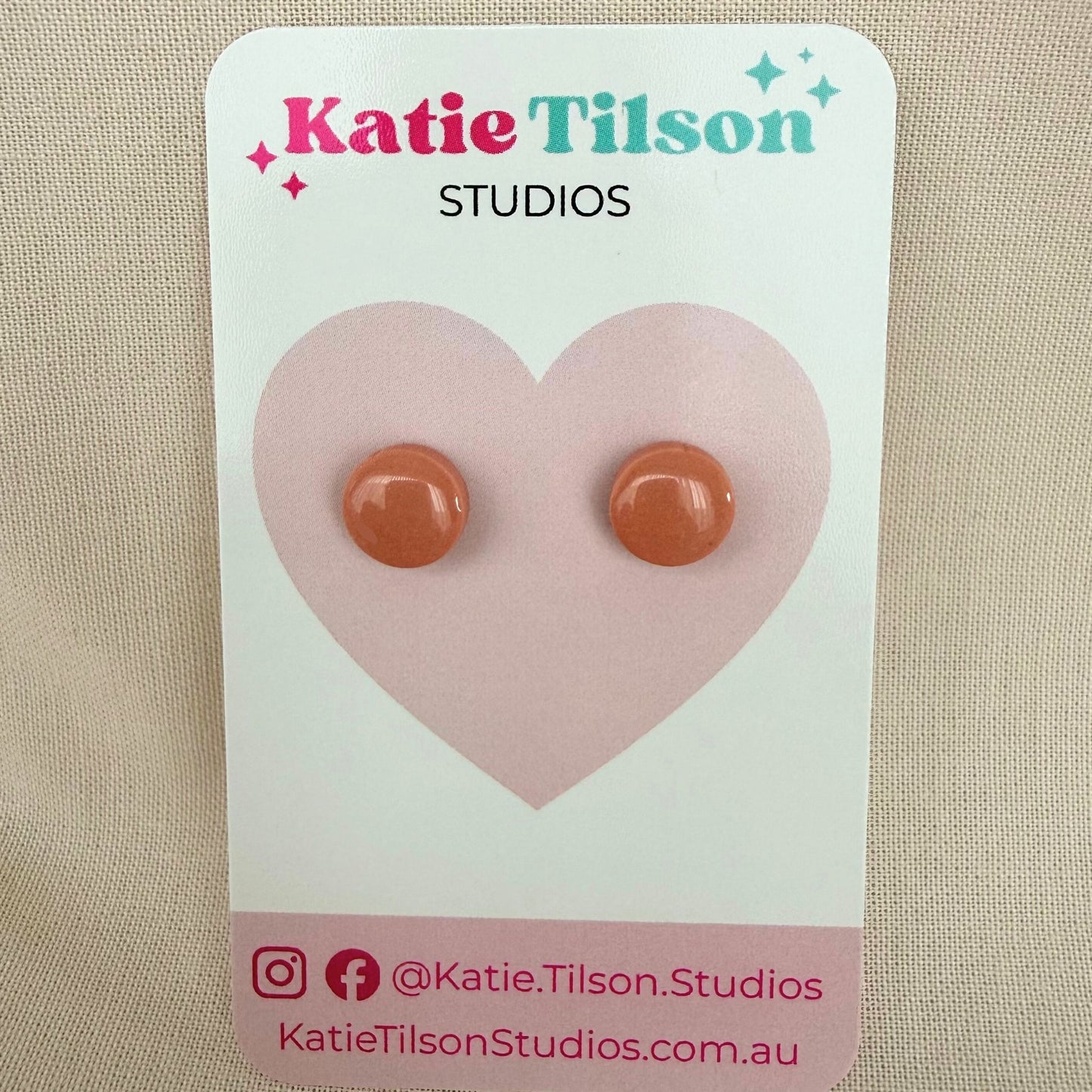 Blush coloured round stud earrings on a Katie Tilson Studios earring card against a beige background.