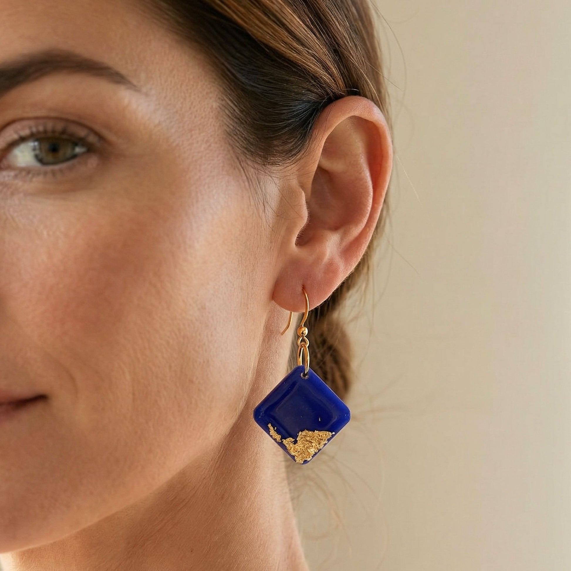 Bright Side square shaped dangle earrings in cobalt blue with gold leaf details and high gloss shine worn on ear.