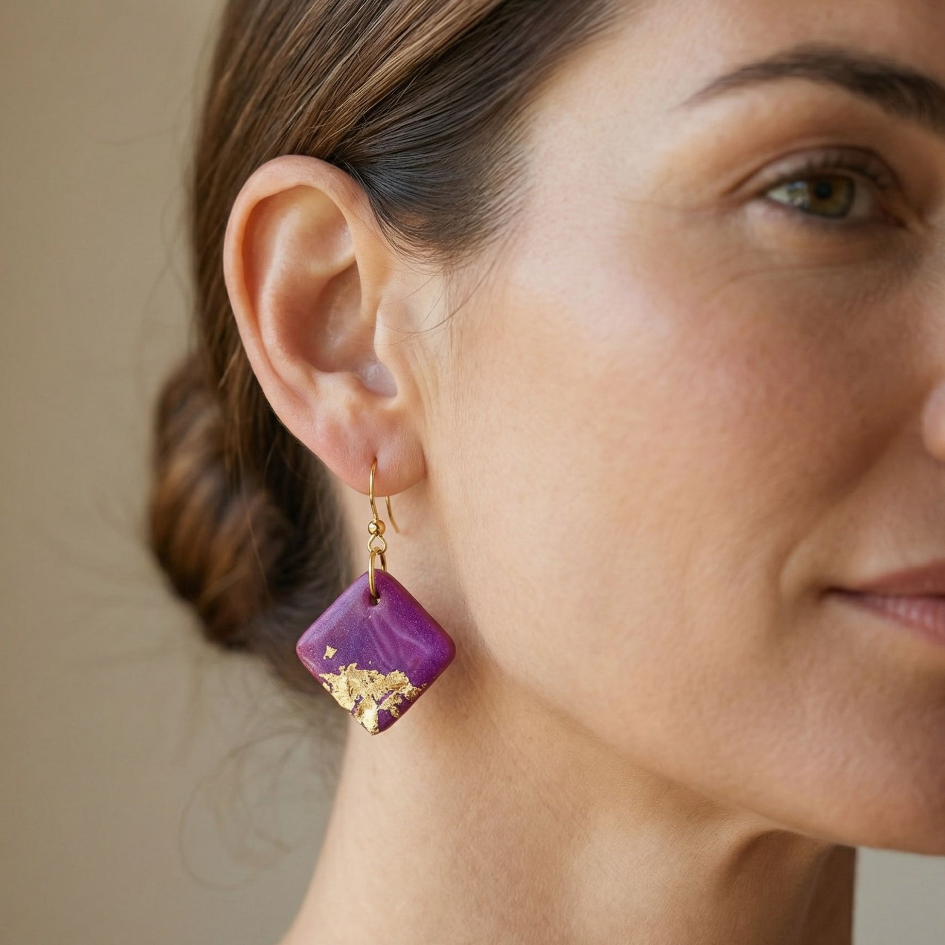 Bright Side handmade dangle earrings in magenta with gold leaf details worn on ear.