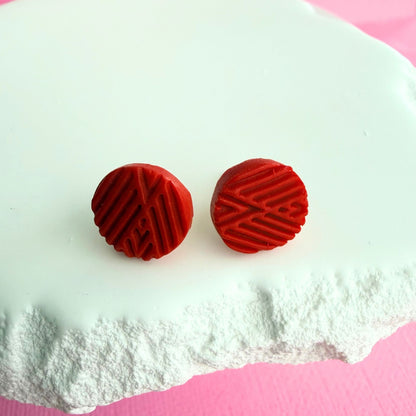 Red textured round stud earrings on a white and pink background.
