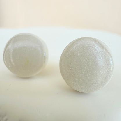 A pair of milky white circle studs with shimmer and glossy resin finish resting on a white surface.