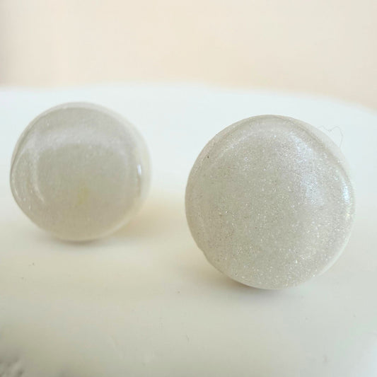 A pair of milky white circle studs with shimmer and glossy resin finish resting on a white surface.